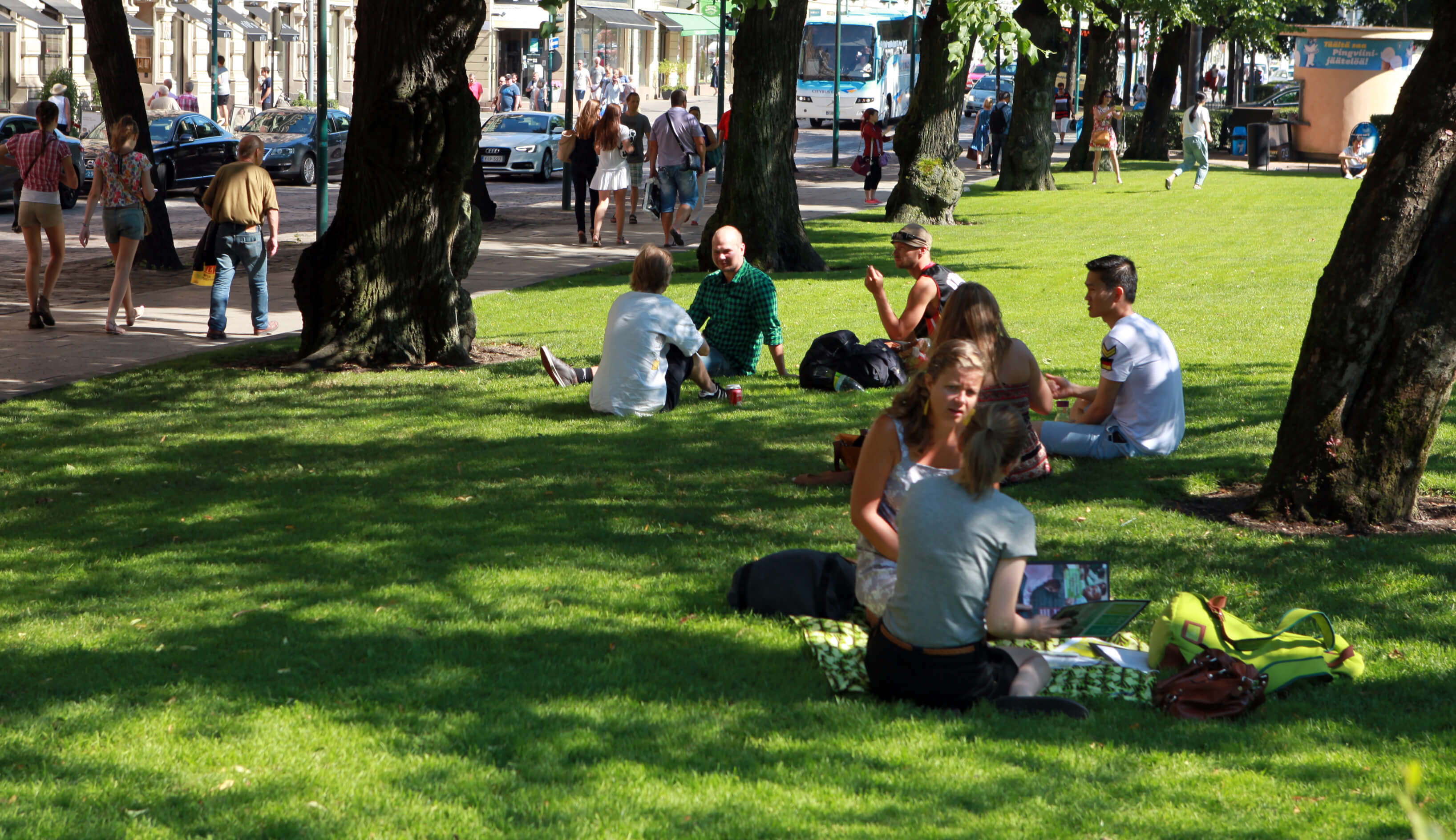 Ihmisiä istuu kaupunkipuistossa kesällä nurmikolla keskustelemassa