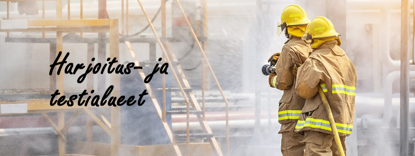 Harjoitus- ja testialueet - kaksi palomiestä pitää vesiletkua kohden savuavaa rakennusta.